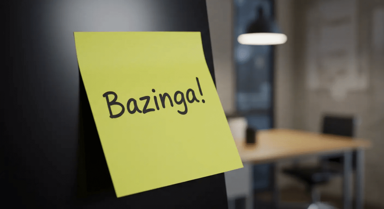 Foto de um post-it com a palavra Bazinga! colado no monitor de um computador de escritório
